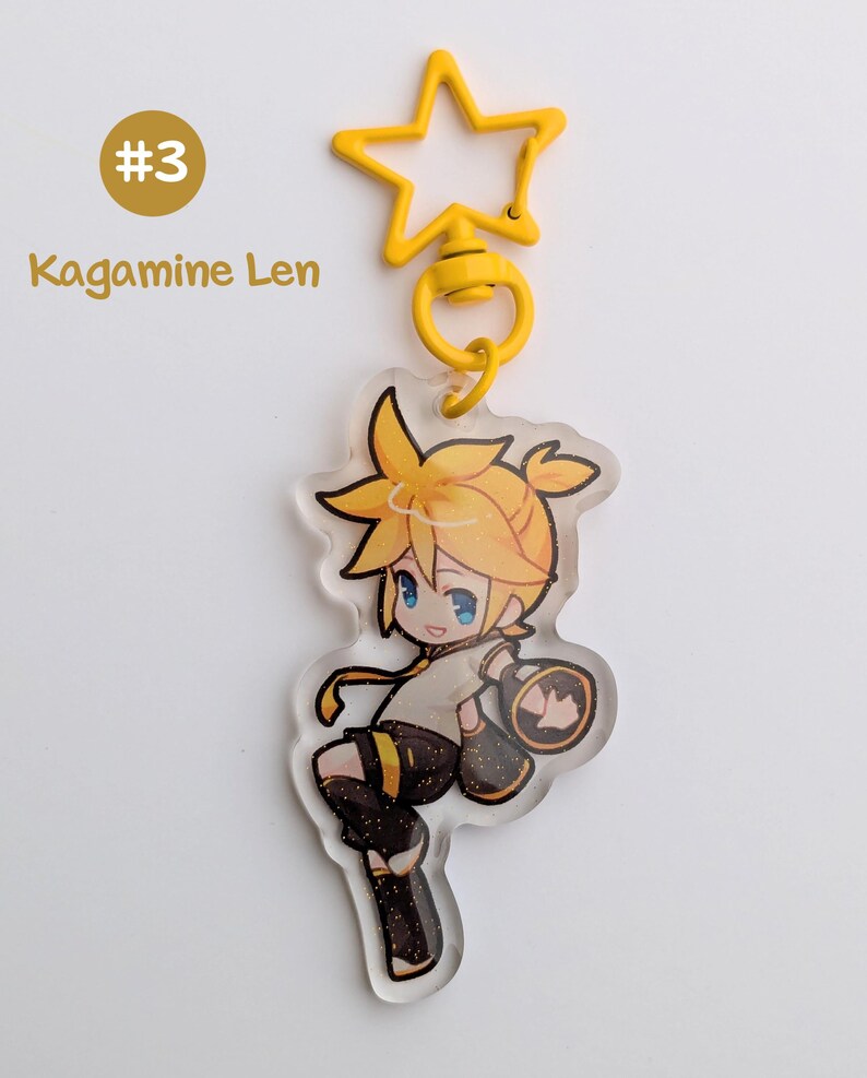 May include: A yellow star-shaped keychain with a cartoon character illustration. The character has yellow hair and blue eyes, wearing a black and gold outfit. The text "#3 Kagamine Len" is visible.