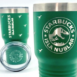 以下が含まれることがあります： 白いロゴに「スターバックス イスラ・ヌブラール」と恐竜のシルエットが描かれた緑色のステンレス製タンブラー。タンブラーには蓋が付いており、小さな恐竜のシルエットで飾られています。