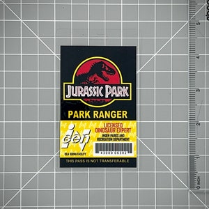 Op de afbeelding: Een gele en zwarte Jurassic Park park ranger ID-kaart met een zwart silhouet van een dinosaurus op een rode cirkel. De tekst op de kaart luidt "Jurassic Park Park Ranger Licensed Dinosaur Expert InGen Parks and Recreation Department Isla Sorna Facility 43000 06302 This Pass Is Not Transferable".