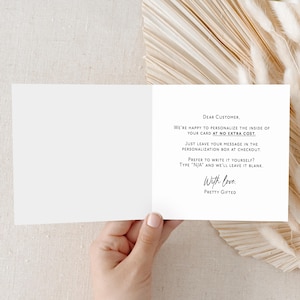 May include: An open, blank greeting card with text that reads "DEAR CUSTOMER, WE'RE HAPPY TO PERSONALIZE THE INSIDE OF YOUR CARD AT NO EXTRA COST." The card is held by a hand and is set against a neutral background.