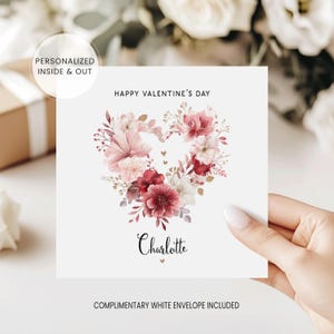 May include: A white Valentine's Day card featuring a heart-shaped floral arrangement in shades of pink and red. The card includes the text "Happy Valentine's Day" and the name "Charlotte".