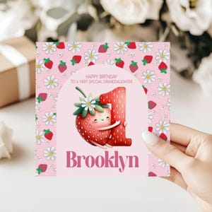 May include: A pink birthday card with a strawberry and the number one. The card has a floral pattern with daisies and strawberries. The text reads "Happy Birthday to a very special granddaughter" and "Brooklyn".