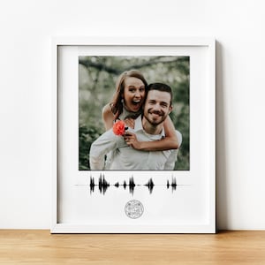 May include: A white frame with a photo of a couple smiling in a forest. The photo is accompanied by a black sound wave graphic and a circular QR code.