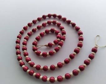 May include: A long strand of wooden beads in shades of red and natural wood. The beads are strung together on a thin cord and are arranged in a circular pattern.