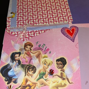 May include: A pink background with a group of five fairies. The fairies are Tinkerbell, Silvermist, Iridessa, Fawn, and Rosetta. The fairies are all wearing their signature outfits and have their wings spread out. The text "Fairies" is written in pink letters at the top of the image. The text "Silvermist" and "Iridessa" are written at the bottom of the image.