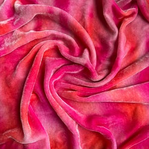 Può includere: Primo piano di un tessuto di velluto rosa e arancione tie-dye. Il tessuto è morbido e ha una sensazione lussuosa.