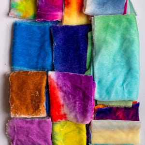 May include: Assortment of colourful velvet fabric scraps in various shades of blue, green, purple, yellow, orange, and brown. The fabric scraps are arranged in a grid pattern.