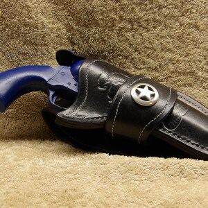 May include: A blue revolver pistol in a black leather holster with a silver star on the strap.