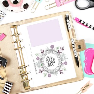 May include: A gold planner is open to a page with a lavender box and a circular floral design with the text "Look For The Good Every Day." Other stationery items include pens, paper clips, and a pink eraser with a pineapple design.