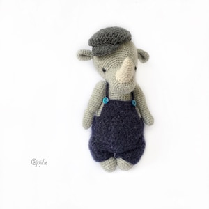 May include: A gray crocheted rhinoceros wearing a gray cap and blue overalls with blue buttons.