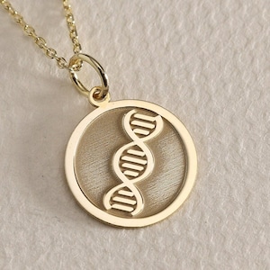 Puede incluir: Un collar de oro con un colgante circular que presenta un diseño detallado de una doble hélice de ADN.