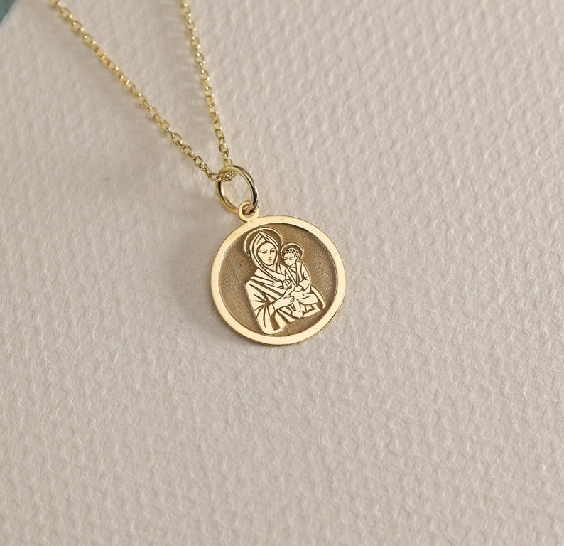 Puede incluir: Un collar de cadena de oro con un colgante redondo que presenta una imagen de la Virgen Mar&iacute;a sosteniendo a un beb&eacute; Jes&uacute;s.
