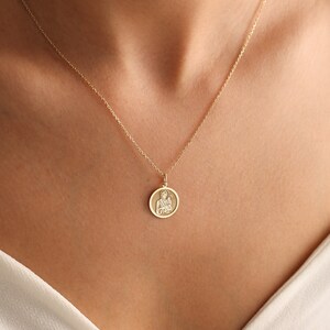 Puede incluir: Un collar de cadena de oro con un colgante redondo que presenta una imagen detallada de la Virgen Mar&iacute;a sosteniendo a un beb&eacute; Jes&uacute;s.