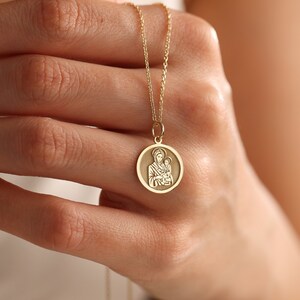 Puede incluir: Un collar de cadena de oro con un colgante redondo que presenta una imagen detallada de la Virgen Mar&iacute;a sosteniendo a un beb&eacute; Jes&uacute;s.