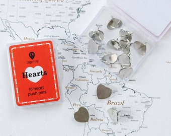 Könnte beinhalten: Herzförmige Reißzwecken in einer transparenten Kunststoffbox, neben einer rot-weißen Karte mit der Aufschrift "Hearts 10 heart push pins". Die Reißzwecken liegen auf einer Weltkarte.