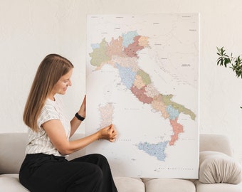 May include: A woman is holding a large map of Italy, which is divided into regions. The map is printed on a white background with black lines and text. The woman is wearing a striped shirt and black pants.