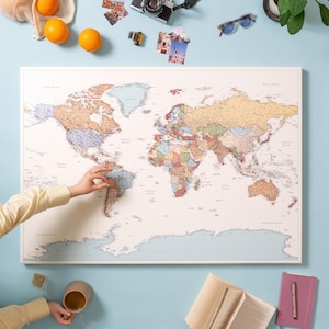 May include: A large rectangular world map with a cream-colored background and pastel-toned continents. The map features numerous small red pins marking various locations across the globe, with a light blue border representing the oceans.