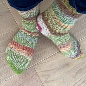 Pode incluir: Um par de meias listradas verdes, laranja e brancas com um padrão de tricô.