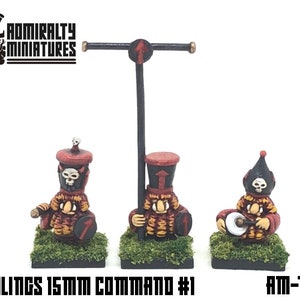 May include: Three 15mm scale miniature figures of goblins, painted in red, black, and yellow. The figures are holding a drum, a spear, and a shield. The figures are on a green base with a black border. The text "T'JUBLINGS 15MM COMMAND #1" and "AM-T1" is visible in the image.