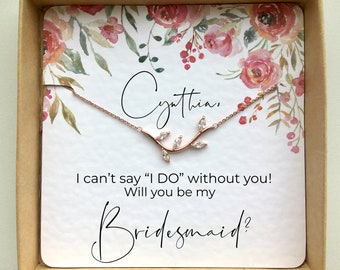 May include: A white card with a floral design and the text "Cynthia, I can't say "I DO" without you! Will you be my Bridesmaid?"  A rose gold necklace with a branch design and small clear stones is displayed on the card.