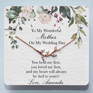 Op de afbeelding: Een witte kaart met een bloemenpatroon en een delicate gouden ketting met een takontwerp. De kaart luidt "To My Wonderful Mother On My Wedding Day You held me first, you loved me first, and my heart will always be tied to yours! Love, Amanda"