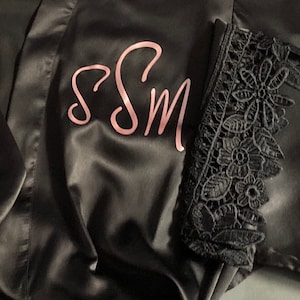May include: Black satin robe with a pink embroidered monogram "SSM" and black lace trim on the sleeves.