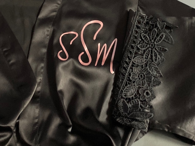 May include: Black satin robe with a pink embroidered monogram "SSM" and black lace trim on the sleeves.