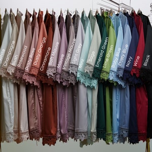 May include: A display of 20 different colored shirts with lace trim on the sleeves. The colors are white, champagne, blush, rosewood, dusty rose, dusty orange, cinnamone, soft mauve, mauve, vintage mauve, light grey, mint, sage, emerald green, lime green, baby blue, dusty blue, navy, wine, and black.