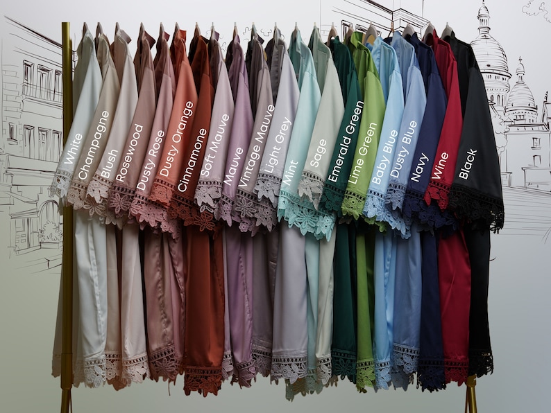 May include: A display of 20 different colored shirts with lace trim on the sleeves. The colors are white, champagne, blush, rosewood, dusty rose, dusty orange, cinnamone, soft mauve, mauve, vintage mauve, light grey, mint, sage, emerald green, lime green, baby blue, dusty blue, navy, wine, and black.