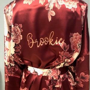 May include: Burgundy satin robe with a floral print and the name "Brookie" embroidered on the back.