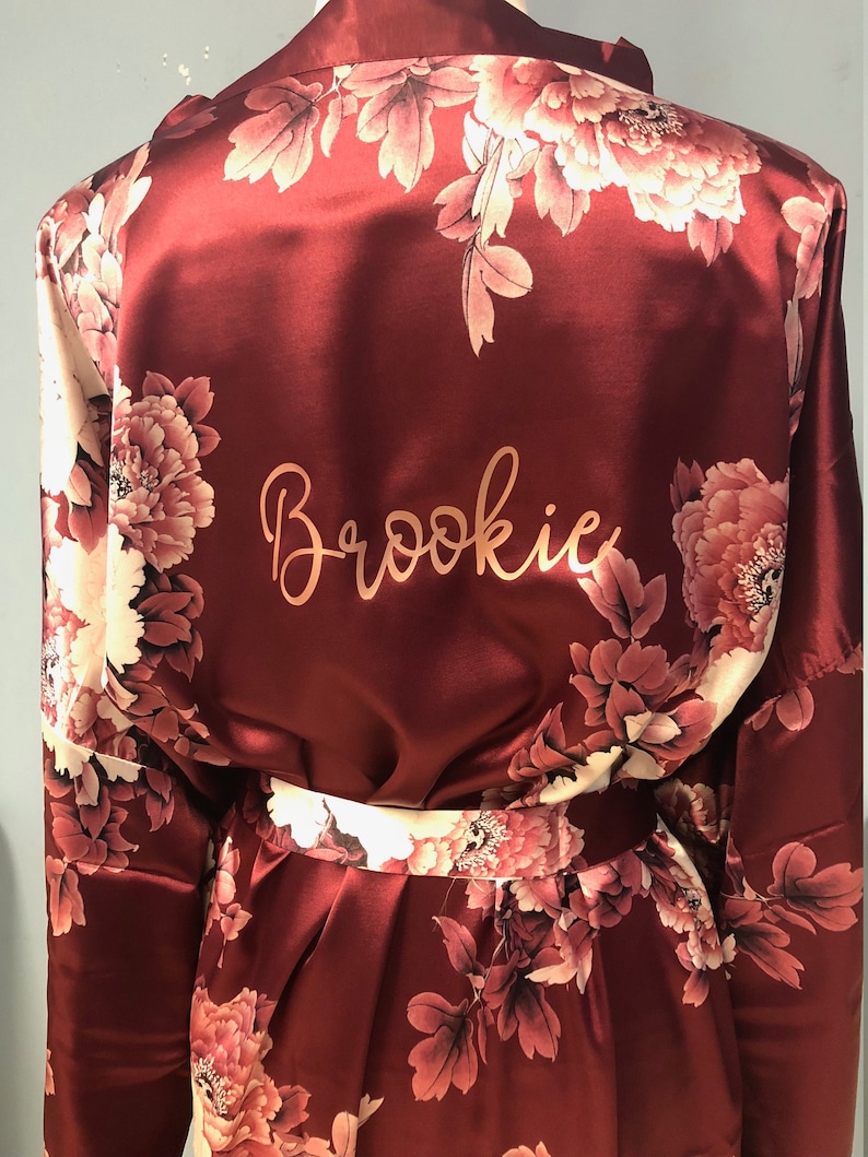 May include: Burgundy satin robe with a floral print and the name "Brookie" embroidered on the back.