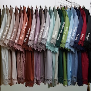 May include: A display of 20 different colored shirts with lace trim on the sleeves. The colors are white, champagne, blush, rosewood, dusty rose, dusty orange, cinnamone, soft mauve, mauve, vintage mauve, light grey, mint, sage, emerald green, lime green, baby blue, dusty blue, navy, wine, and black.