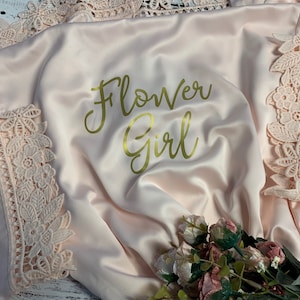 May include: A pink satin robe with gold lettering that says "Flower Girl" and lace trim.