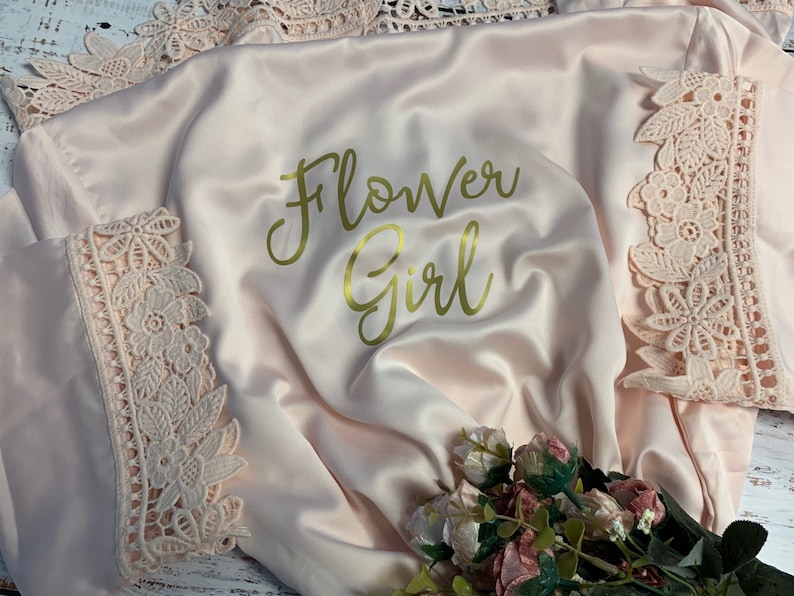 May include: A pink satin robe with gold lettering that says "Flower Girl" and lace trim.
