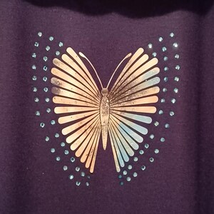 May include: A dark purple shirt with a butterfly design in tan and light blue, and small blue accents. The shirt has the text "Daddy2Design" across the top. A patterned scarf is draped over the shirt.