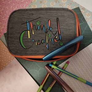 Könnte beinhalten: Eine graue Stiftebox mit Reißverschluss und dem Schriftzug "Think Creative" in bunten Buchstaben. Die Box ist von bunten Stiften und Bleistiften umgeben.