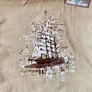 Könnte beinhalten: Ein beiges Kissen mit einer braunen Schiffgrafik und Text, der "Sail Away" und "Ocean" sagt. Das Kissen hat ein Etikett, auf dem "Ich teste für Daddy2Design" steht.