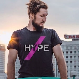 Könnte beinhalten: Eine Person trägt ein schwarzes T-Shirt mit einem pinkfarbenen diagonalen Schrägstrich und dem Wort "HYPE" in weißen Buchstaben. Die Person hält ein blaugrünes und weißes Longboard mit dem Wort "Summer" darauf.