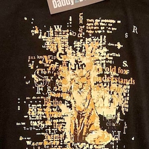 Könnte beinhalten: Schwarzes T-Shirt mit einem goldenen Grafikdruck eines Fuchses. Die Grafik besteht aus überlappendem Text, darunter der Satz "An old fox understands". Der Text "Ich teste für Daddy 2 Design" ist auf einem weißen Etikett aufgedruckt, das am Shirt befestigt ist.