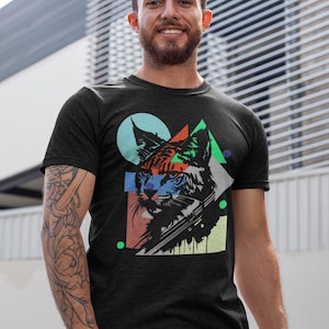 Könnte beinhalten: Schwarzes T-Shirt mit einer grafischen Katzenzeichnung. Das Gesicht der Katze ist mit geometrischen Formen in Türkis, Rot, Grün und Blau dargestellt. Das T-Shirt ist kurzärmlig.