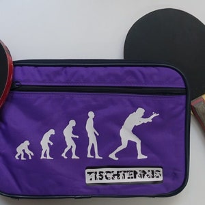 May include: Purple table tennis bag with a zipper closure. The bag features a white silhouette of the evolution of humans playing table tennis. The text "TISCHTENNS" is printed on the bag. The bag is next to a black table tennis paddle with a wooden handle.