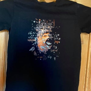 Könnte beinhalten: Schwarzes T-Shirt mit einem grafischen Aufdruck eines Löwenkopfes mit den Worten "Leone", "Love" und japanischen Schriftzeichen.