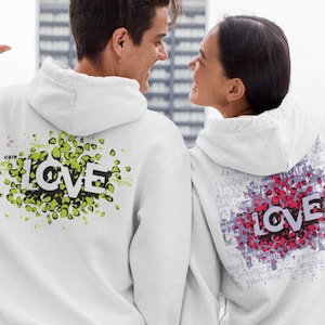 Puede incluir: Dos sudaderas con capucha blancas con un estampado gráfico de la palabra "LOVE" en un diseño abstracto y colorido. El diseño de la sudadera con capucha de la izquierda es verde y negro, mientras que el diseño de la sudadera con capucha de la derecha es rosa y morado.