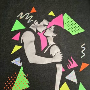 Könnte beinhalten: Dunkelgrauer Kapuzenpullover mit einer Grafik eines sich küssenden Paares, umgeben von neonrosa, grünen, orangefarbenen und gelben geometrischen Formen. Das Design hat einen Retro-80er-Jahre-Vibe.