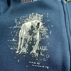 May include: A dark blue hooded sweatshirt with a white polar bear graphic and the text "Daddy2Design" printed on the front.