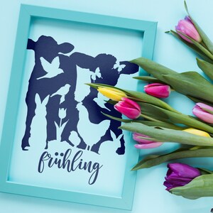 Könnte beinhalten: Ein blauer gerahmter Druck mit einer Silhouette einer Kuh, eines Schafes, eines Huhns, eines Kaninchens und Vögeln. Der Druck sagt "frühling". Der Druck ist von einem Strauß rosa, gelber und lila Tulpen umgeben.