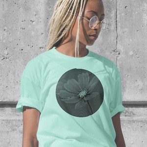 Könnte beinhalten: Hellblaues T-Shirt mit einem großen schwarzen Spiralmuster. Das Design ist mittig platziert und bildet einen auffälligen Kontrast. Das T-Shirt hat kurze Ärmel und eine lockere Passform.