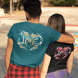 May include: Two t-shirts, one teal and one black, each featuring a heart design with the word "LOVE" in a stylized font. The teal shirt has a red and black plaid pattern at the bottom. The black shirt has a purple and black plaid pattern at the bottom.
