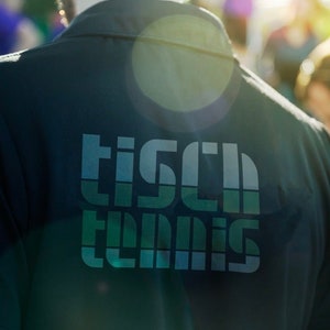 May include: A dark green shirt with a white and blue graphic that says "Tisch Tennis" on the back.
