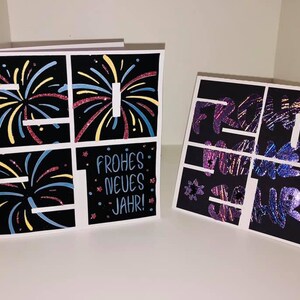 Puede incluir: Dos tarjetas negras con borde blanco. La tarjeta de la izquierda tiene una cuadr&iacute;cula de cuatro cuadrados con ilustraciones de fuegos artificiales en cada cuadrado. La tarjeta de la derecha tiene una cuadr&iacute;cula de cuatro cuadrados con el texto "Frohes Neues Jahr!" en cada cuadrado. El texto est&aacute; en una fuente brillante e iridiscente.